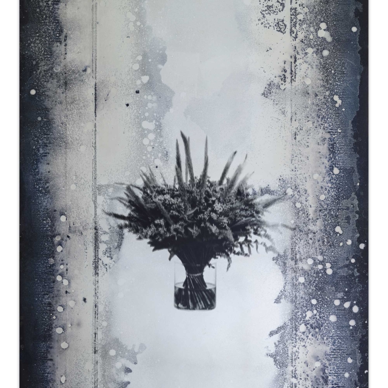In the picture we see a mirror with a bunch of flowers in the middle.
The edges are dark and speckled, like an old photo or film.
The work of art is by Andreas Duscha.
He made the mirror himself, following an old recipe from the 17th century.
In the middle you can see an arrangement of flowers - it is a screen print on the mirror surface.
The flowers on the mirror have a deeper meaning:
They stand for social crises and revolutions.
A bouquet is a reminder of revolutions, for example: the Carnation Revolution in Portugal or
the Tulip Revolution in Ukraine.
Duscha is interested in hidden stories and connections.
He uses old techniques and special materials,
to make themes such as power, change and history visible in a quiet, poetic way.
This artwork is part of a series of four mirrors,
, which hang in the anteroom of the Heidi Horten Collection museum toilets.
Each mirror tells its own story - through plants and symbols.