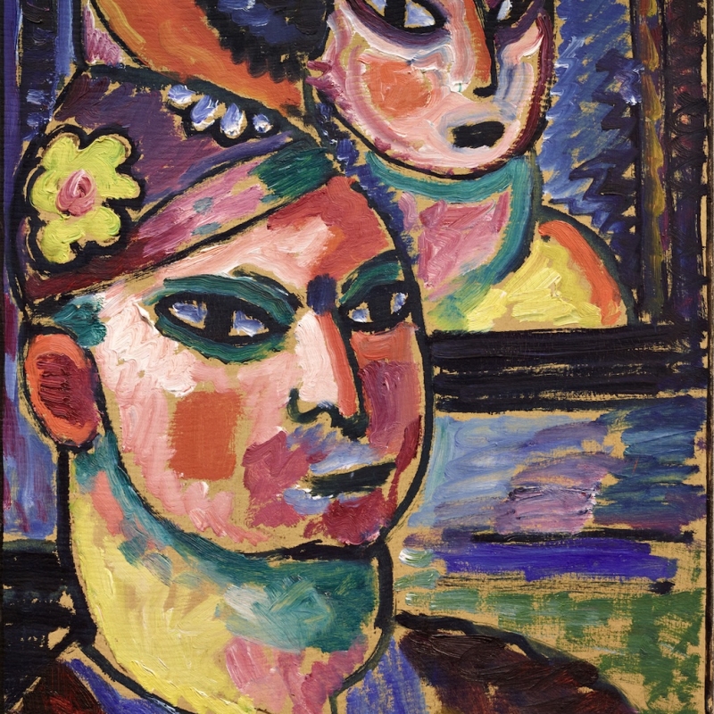 Das expressionistische Gemälde zeigt zwei stilisierte Porträts: Im Vordergrund ist ein männliches Gesicht mit stark betonten schwarzen Augen, roten und rosafarbenen Wangen sowie grün-blauen und gelben Farbflächen zu sehen. Die Konturen des Gesichts sind dick und schwarz umrissen. Der Blick ist ernst und geradeaus gerichtet. Auf dem Kopf trägt die Figur eine Kappe mit einer gelben Blume an der Seite.
Im Hintergrund ist ein zweites Gesicht – vermutlich eine Frau – in einem rechteckigen Rahmen dargestellt, als sähe man ein Bild im Bild oder eine Spiegelung. Auch ihr Gesicht ist flächig und expressiv mit kräftigen Farben gemalt: rosa, orange, grün und blau dominieren. Beide Figuren haben große mandelförmige Augen mit dunklen Umrandungen. Der Hintergrund ist farbintensiv und lebendig – mit Pinselstrichen in Blau, Violett und Goldocker.
Die Malweise ist energisch, mit sichtbaren Pinselzügen und kontrastreichen Farbflächen. Die Darstellung wirkt bewusst unnatürlich, symbolisch und emotional aufgeladen – typisch für den Expressionismus um 1912.