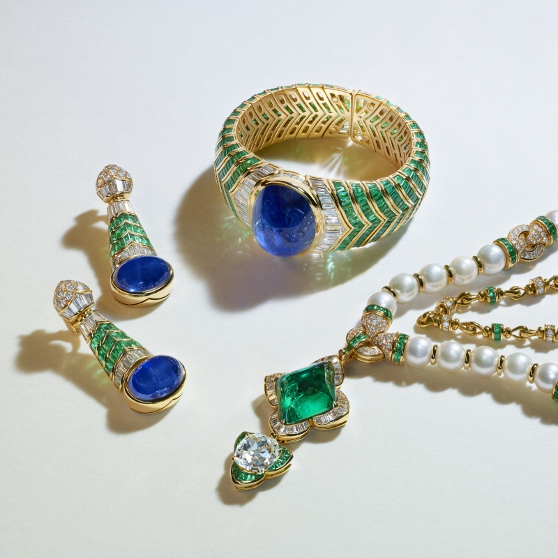 Gold jewelry set featuring a bracelet, earrings, and necklace adorned with blue stones, green accents, and pearls.