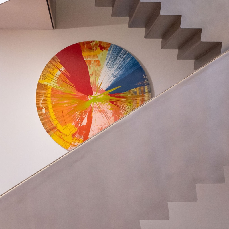 Blick auf eine moderne Treppe mit einem bunten, runden Kunstwerk an der Wand.