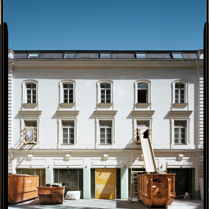 Construction site featuring a white building, orange dumpsters, and a wooden ramp leading to an upper window.