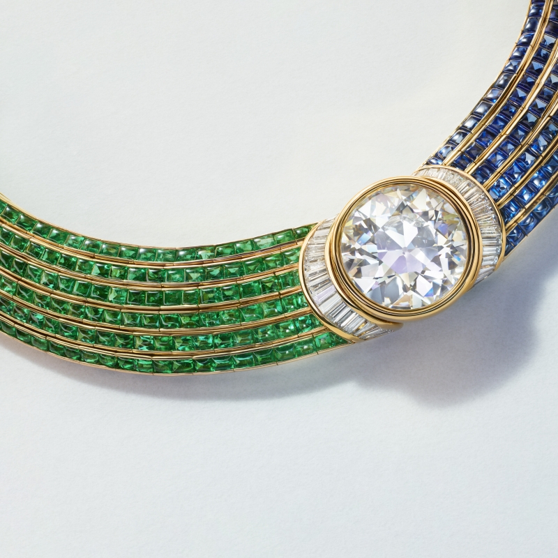 A luxurious necklace featuring green and blue gemstones, with a large central diamond and intricate gold detailing.