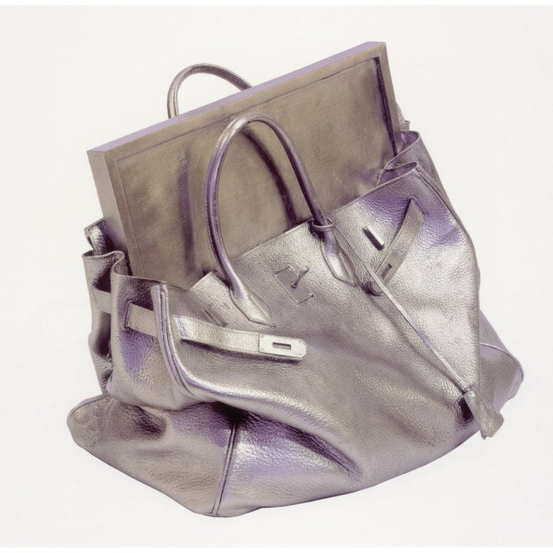 A metallic silver handbag with a rectangular, flat object partially protruding from the top.