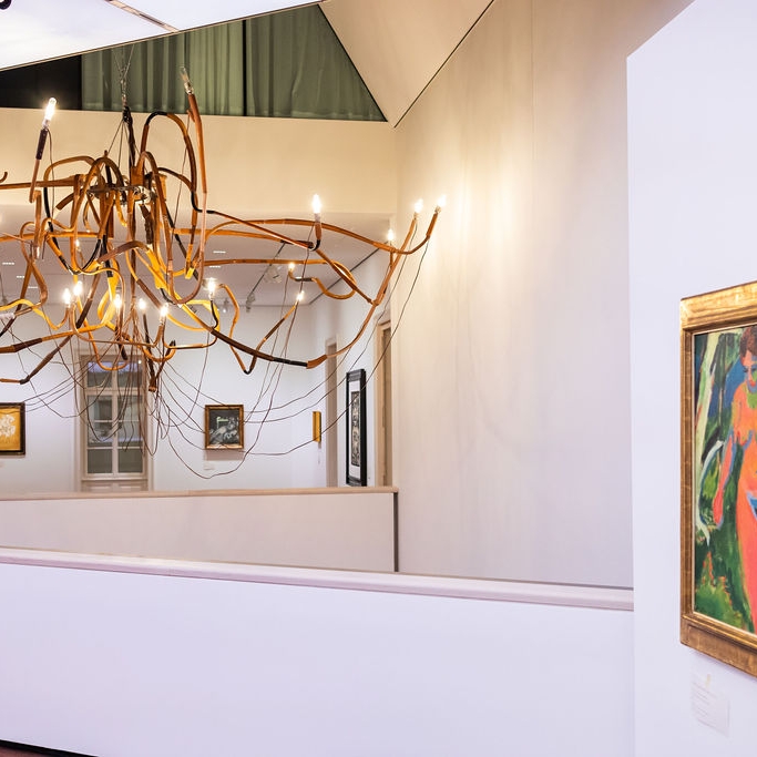 Moderne Galerie mit kunstvollem Kronleuchter und farbenfrohem Gemälde von zwei Frauen an der Wand.