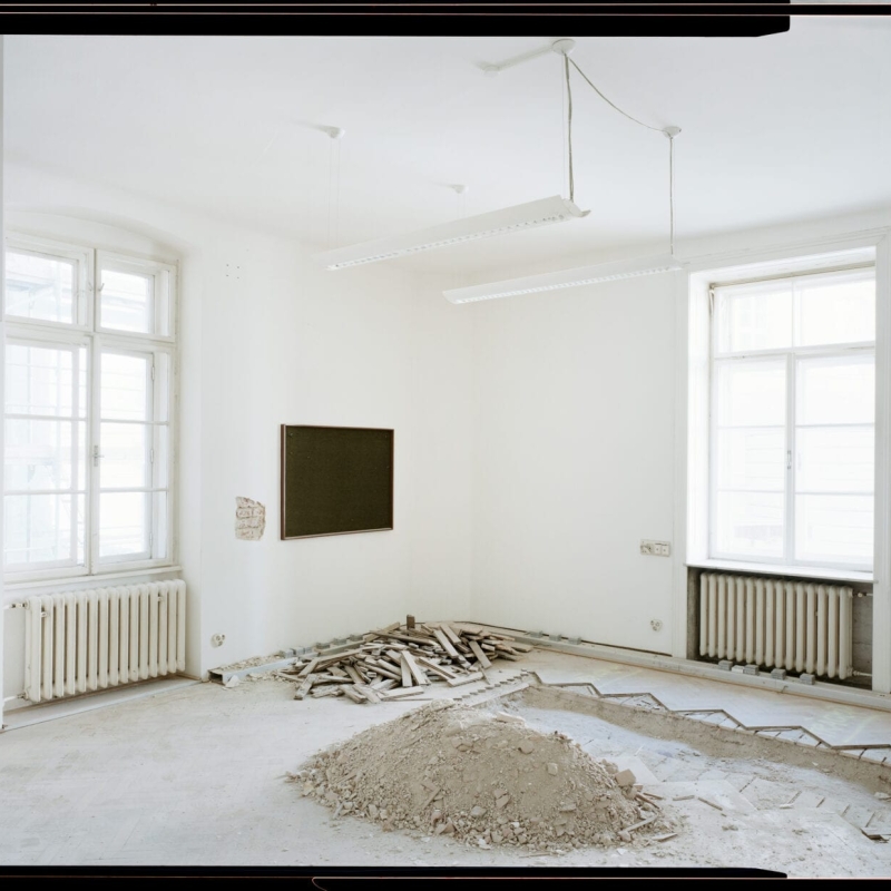 Renovation scene in a bright room with a blackboard, exposed floor, and piles of wood and dust.