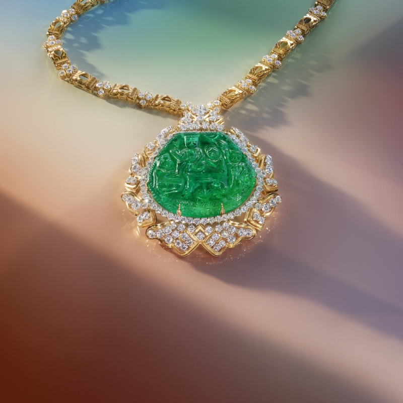 Gold necklace featuring a large green gemstone pendant surrounded by sparkling diamonds.