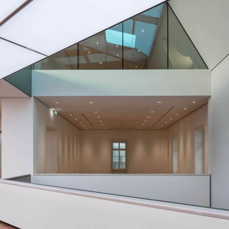 Modern interior with angular architecture, glass elements, and soft lighting, featuring a spacious, minimalist gallery.